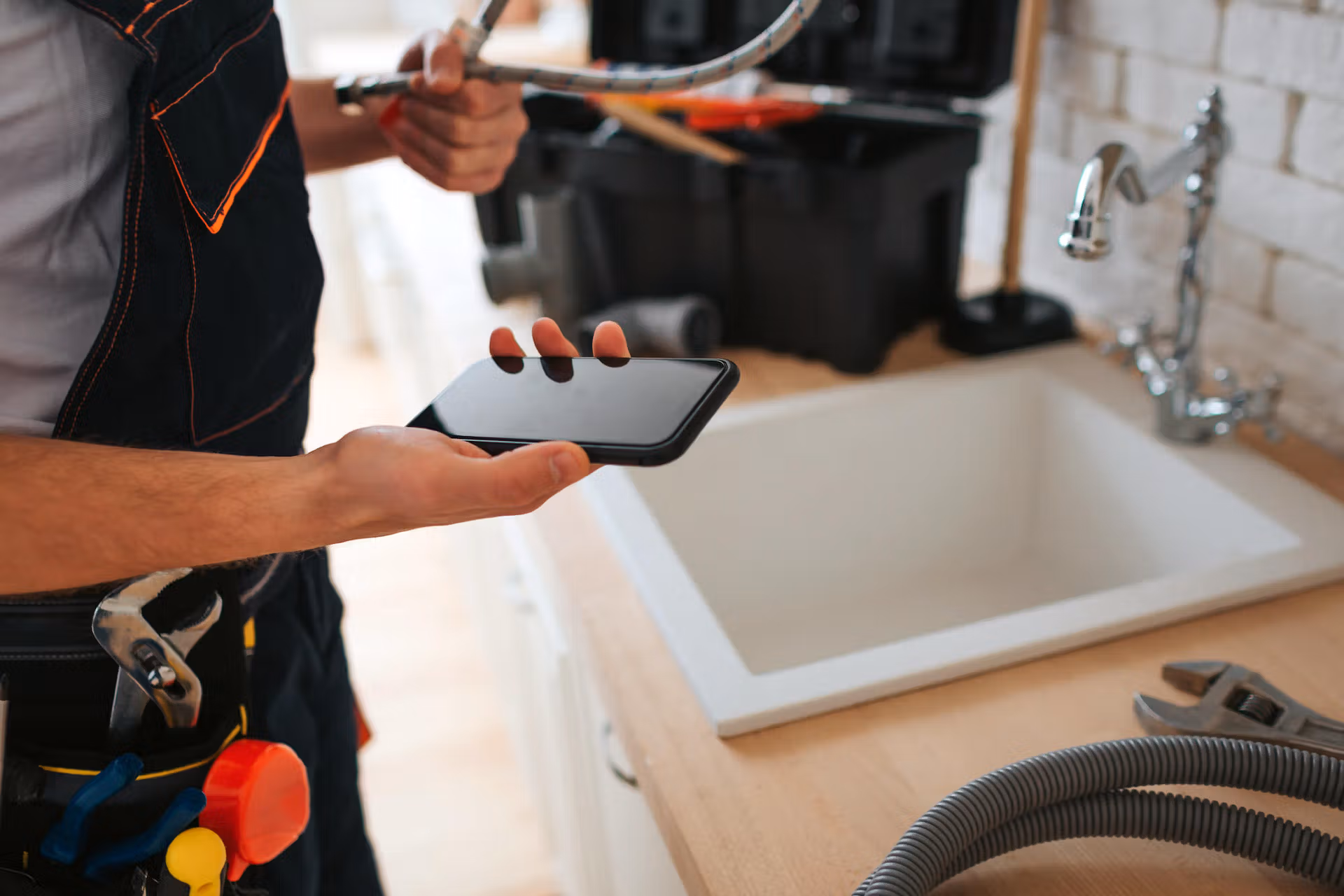 A man beside a sink holds a cell phone in his hand, appearing engaged with the screen as he stands upright.