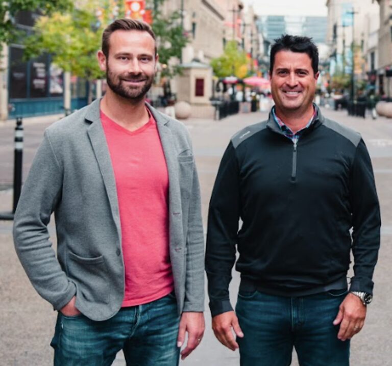 Luke Krueger and Guillermo Salazar standing in the middle of a lively city street, with shops and traffic visible around them.