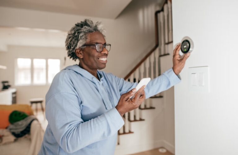 A woman in a blue shirt displays a smart thermostat, highlighting its modern technology and user-friendly interface.