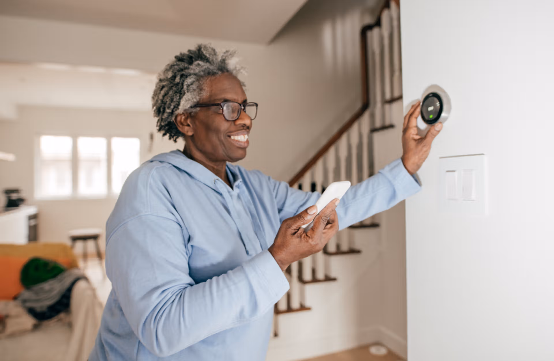 A woman in a blue shirt displays a smart thermostat, highlighting its modern technology and user-friendly interface.