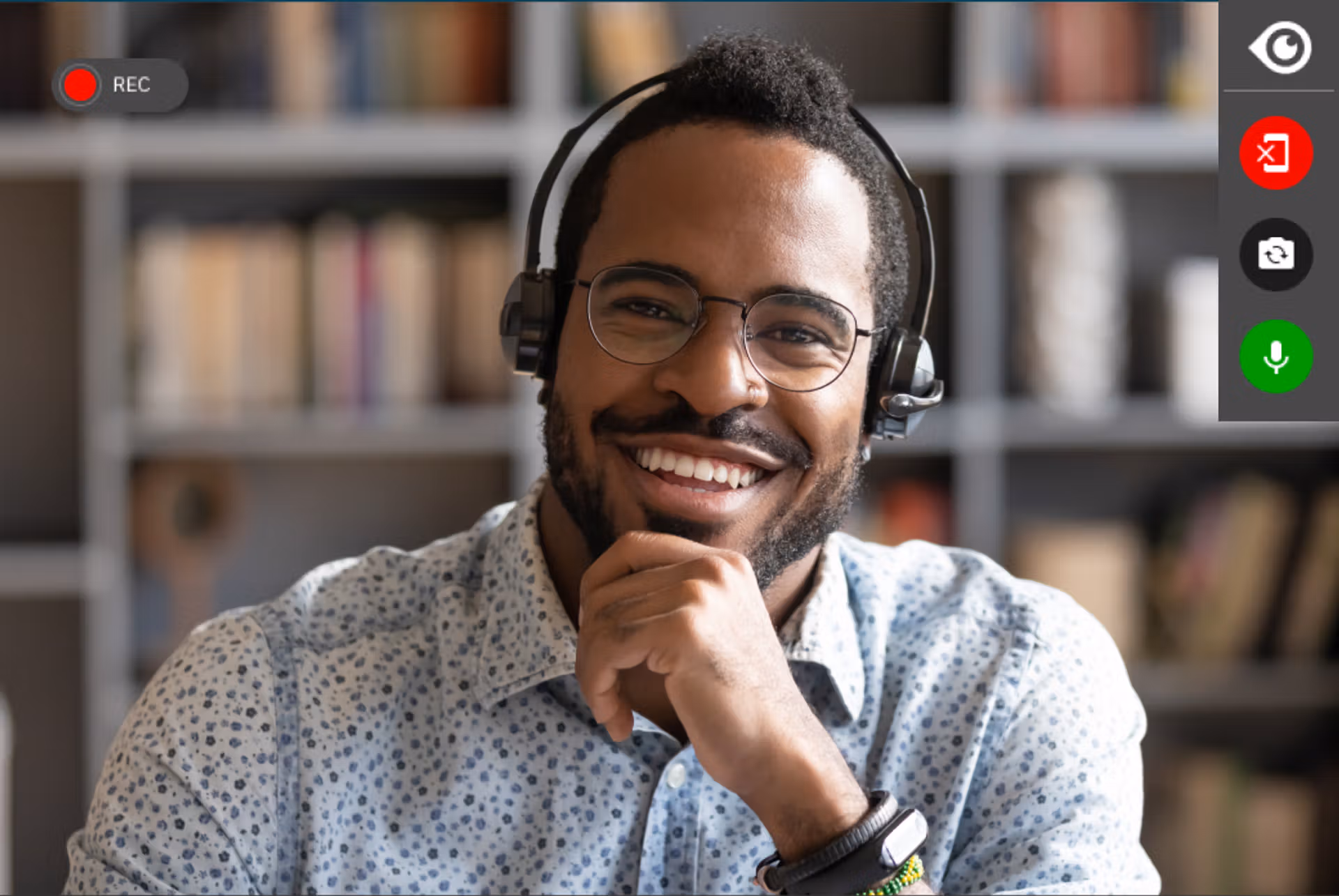 A smiling man wearing headphones sits in front of a computer screen, engaged and enjoying his activity.