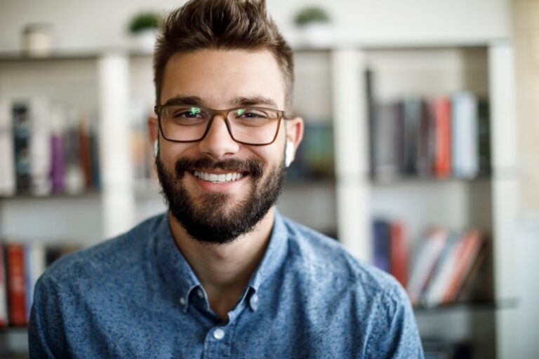 A cheerful man with glasses and a beard smiles at the camera, radiating friendliness and approachability.