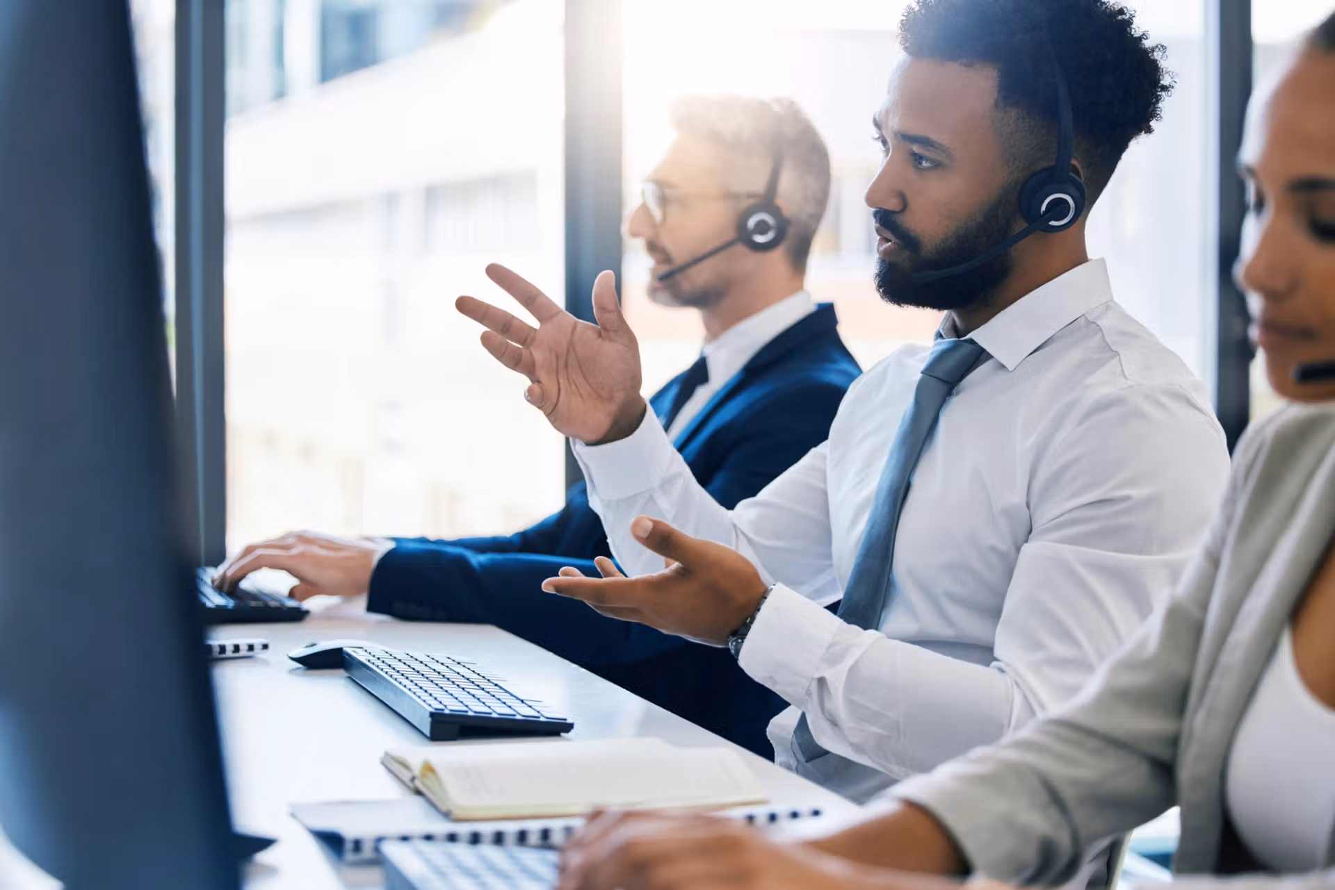 A team of call center representatives collaborating at their desks, each using a headset and computer in a lively office environment.