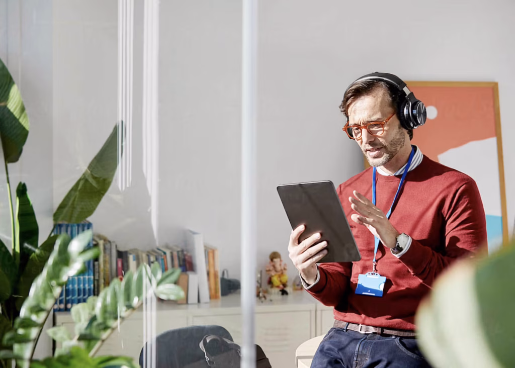 A man wearing headphones, focused on a tablet computer he is holding in his hands.