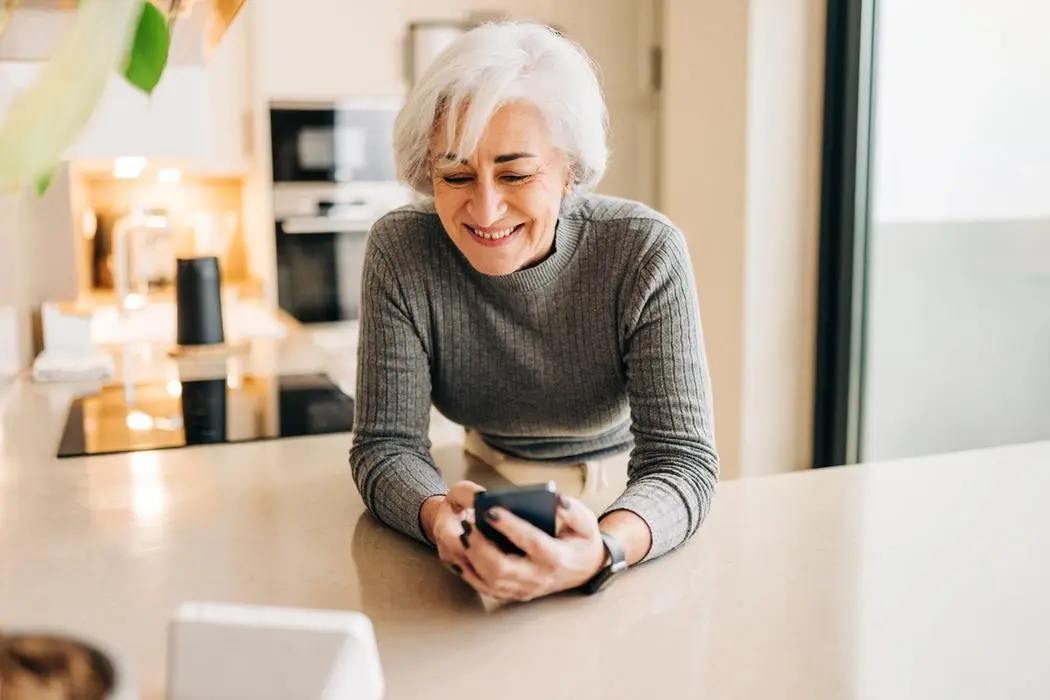 An older woman gazes thoughtfully at her smartphone, engaged in a moment of reflection or communication.