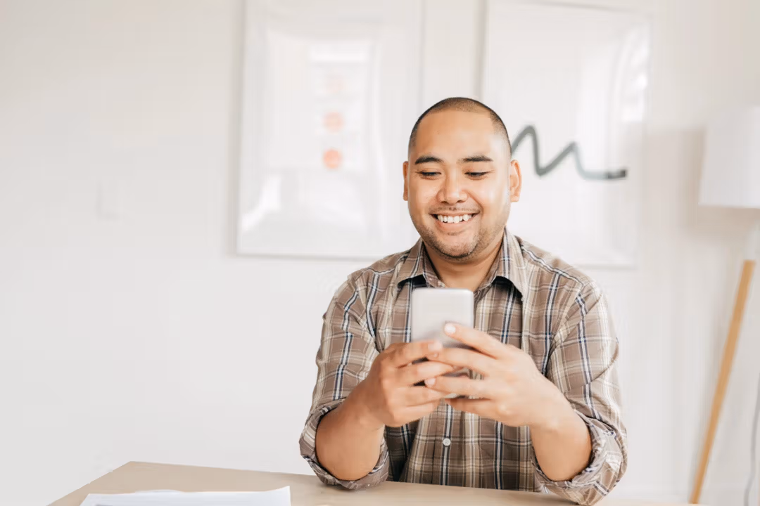 man smiles while engaging with his phone, showcasing a moment of joy and connection in a digital world.