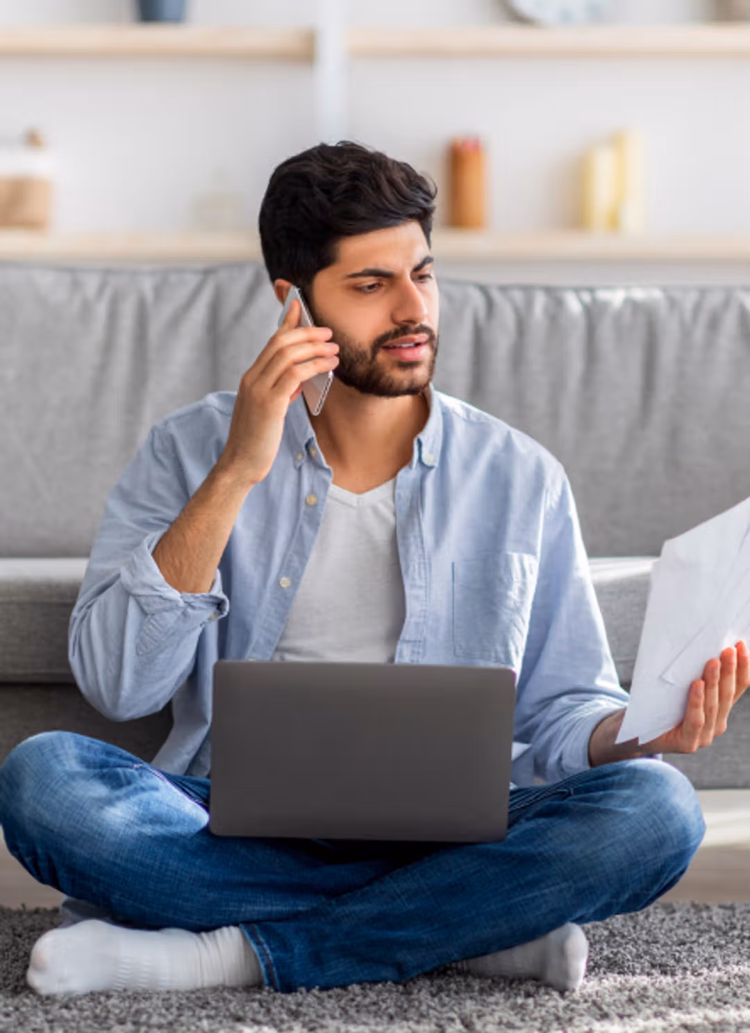 A man sitting on the floor, focused on his laptop, with documents nearby.