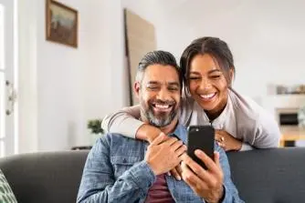 A man and woman sit together on a couch, both focused on their cell phone, sharing a moment of connection.