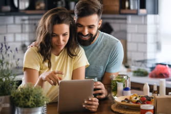 A man and woman in a kitchen, focused on a tablet, sharing ideas and information together.